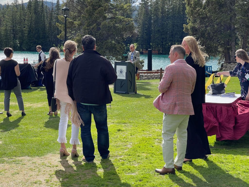 people outside listening to a speaker at a podium with trees in background