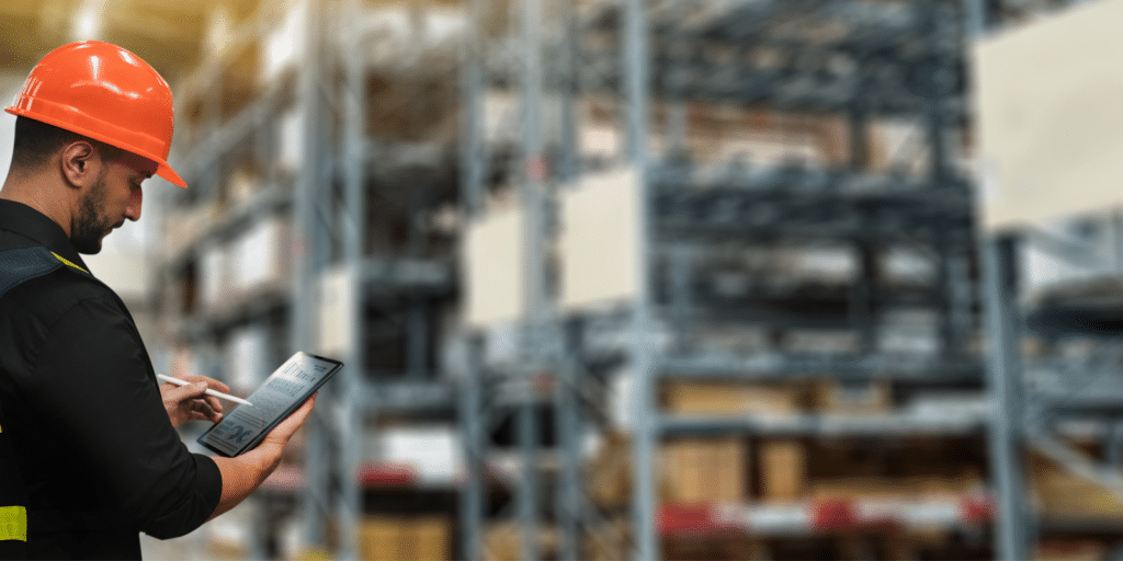 worker in warehouse using digital tablet, wearing a hard hat
